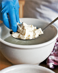 Submerging a spoonful of curds into a ceramic pot of hot water