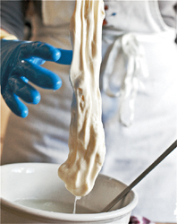 Lifting a large, dangling mass of stretchy cheese from a ceramic pot of hot water