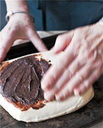 Spreading the cocoa paste over the top of a rectangular block of cheese