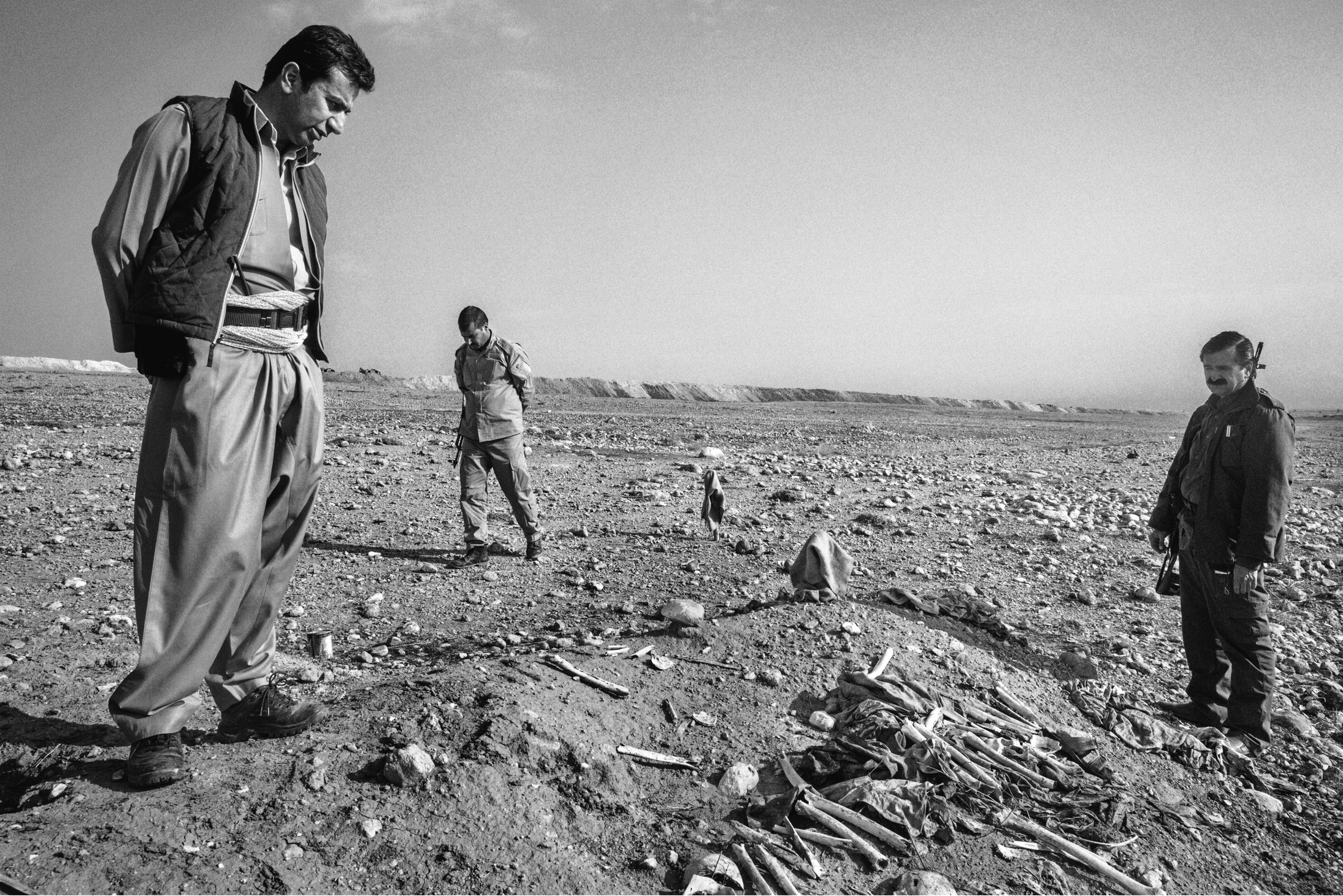 IRAQ. Sinjar. 2015. Dr Azar, left, looks at a mass grave around the town of Sinjar. The border city of Sinjar was liberated after over one year of ISIS occupation in mid november by a joint operation involving 7,500 Kurdish and Yazidi peshmerga and coalition airstrikes. Vast parts of the city are completely destroyed.