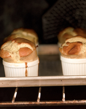 Goat cheese soufflés popping out of ramekins on a baking sheet in an oven