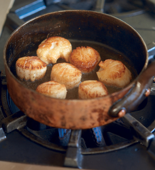 A large copper pan in which scallops are being sautéed