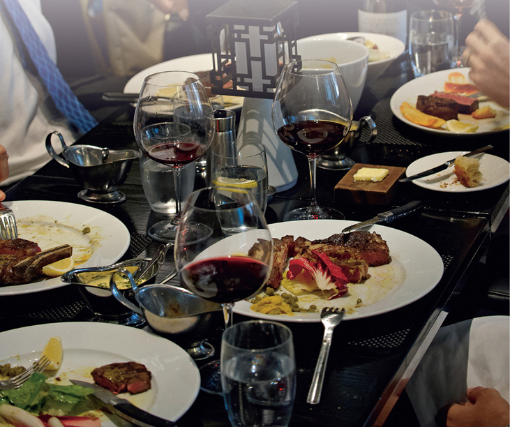 color image of a group of people at a restaurant enjoying WAGYU CHUCK BRAISED IN RED WINE WITH GREMOLATA AND POTATO PUREE along with some half empty glasses of red wine. Must be nice.