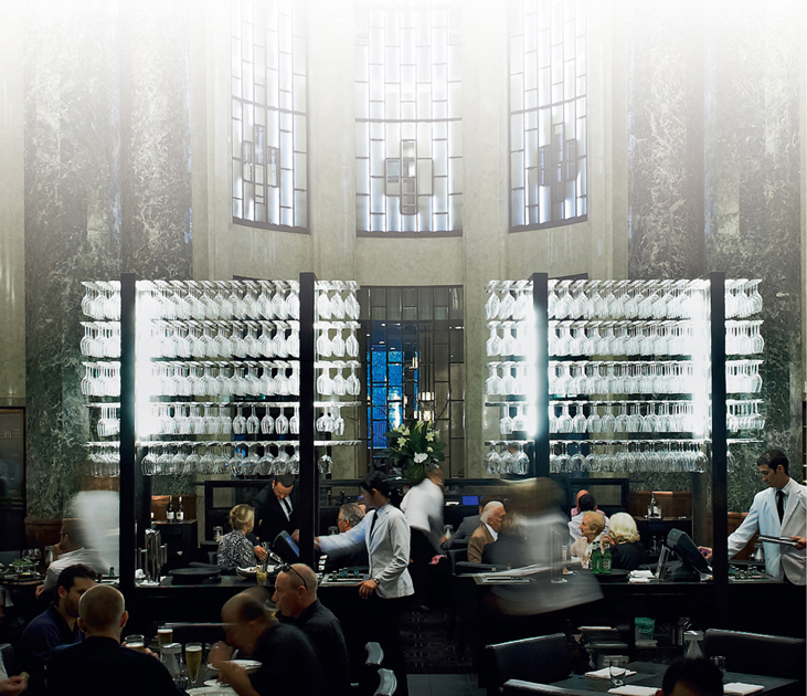 color image of a modern restaurant setting with various people dining along with some waiters and waitresses.