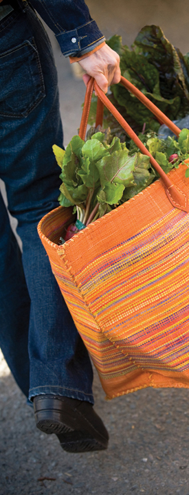 A person walking and carrying a bright cloth tote full of vegetables