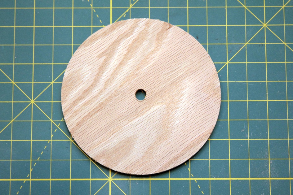 Cut a 4” disk from 1/4” plywood. Drill a hole 9/32” in diameter to accommodate the smaller brass tube.