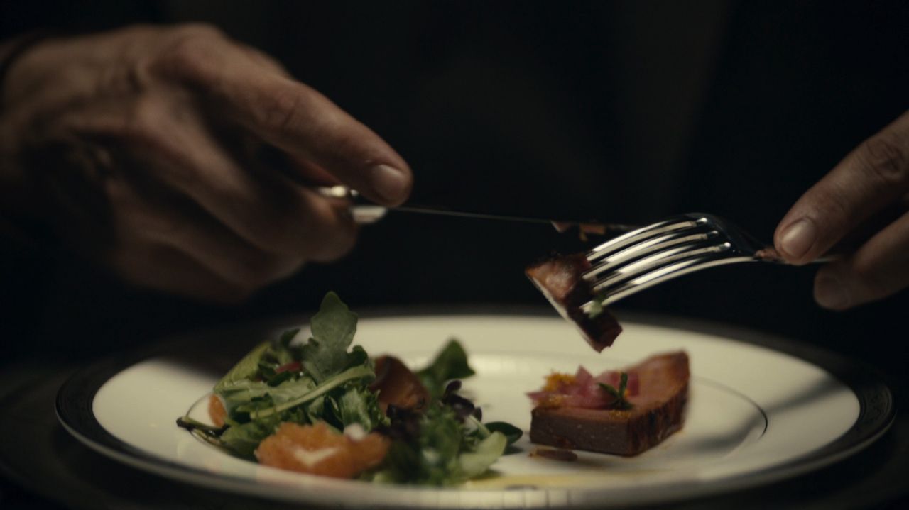 Frame from the Hannibal pilot with Hannibal Lecter’s hands above a plated meal.