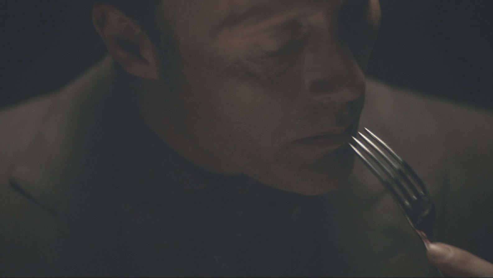 Frame from the Hannibal pilot with Hannibal Lecter in shadow eating his forbidden meal.