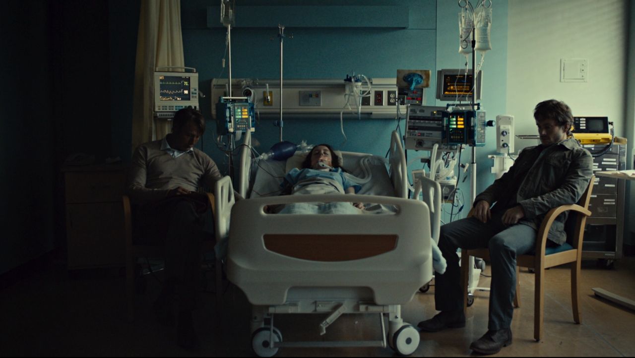 Frame from Hannibal pilot showing Will Graham and Dr. Hannibal Lecter in a hospital room flanking a young woman they saved.