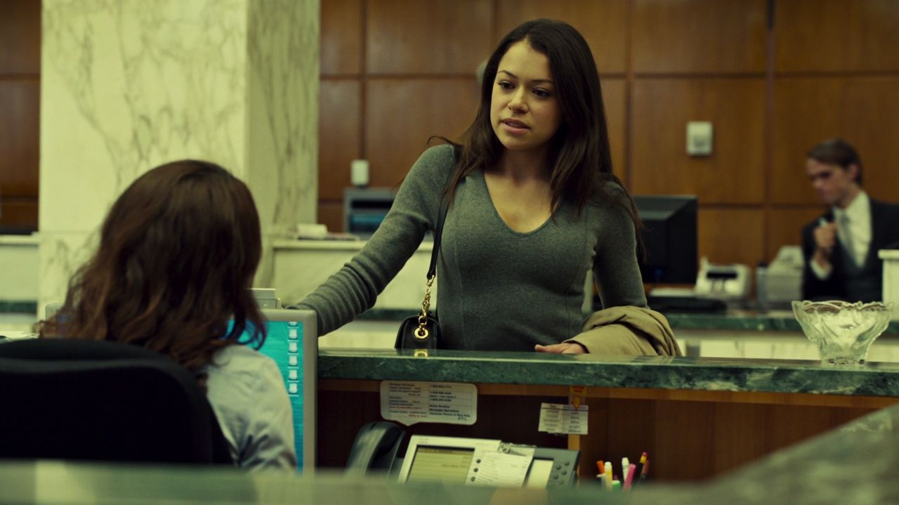 Frame from Orphan Black pilot with Sarah Manning impersonating her lookalike suicide victim Beth Childs in a bank lobby.