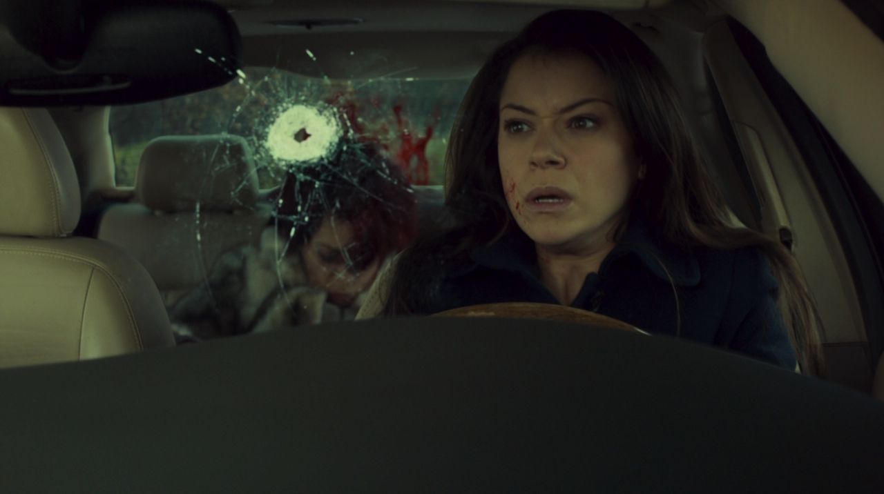 Frame from Orphan Black pilot with Sarah Manning in a car, a new bullet hole in the windshield and another lookalike dead in the backseat.