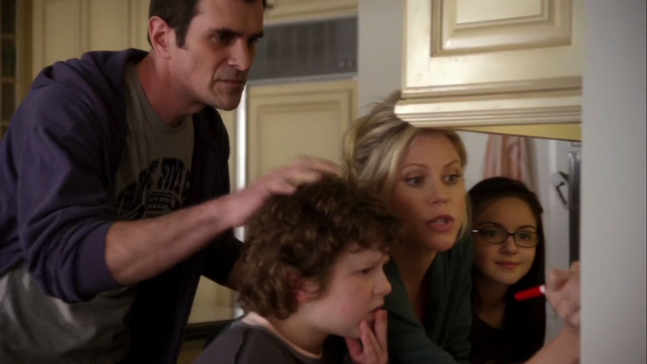 In frame from Modern Family pilot, the Dunphy family crowd around a calendar in the kitchen.