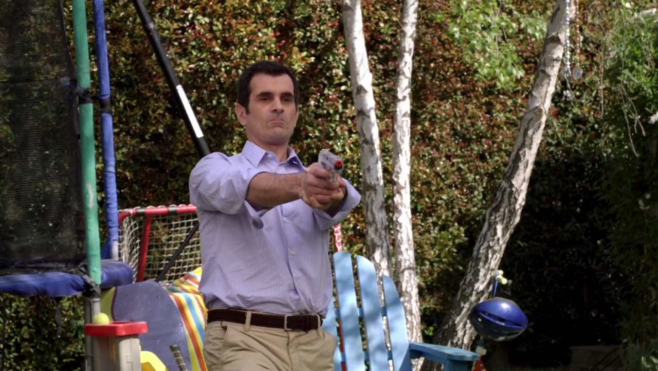 In frame from Modern Family pilot, Phil Dunphy takes aim at his pre-teen son with an Airsoft pistol.