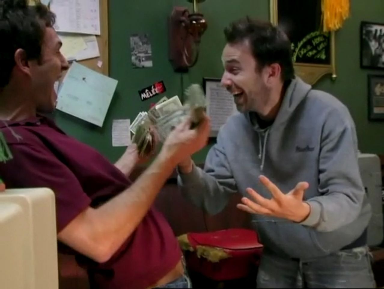 In frame from It’s Always Sunny pilot, Dennis and Charlie celebrate the bar’s new success with stacks of cash.