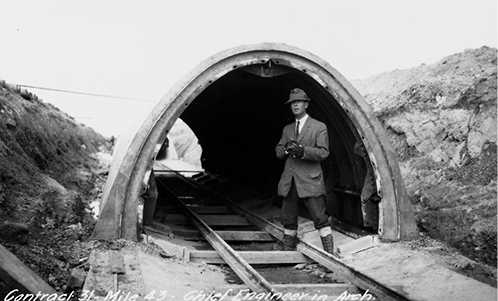 Black and white photograph of W.G. Chance standing inside a small section of aqueduct, flanked by hills on either side. A rail track runs through the centre of the aqueduct channel.