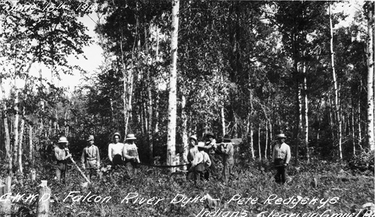 Black and white photograph taken at some distance of a group of Annishinabe men working in a forest; at the centre two workers seem to be cutting down a tree with a long saw while seven other workers stand close by. White script at bottom: G.W.W.D. Falcon River Dyke – Pete Redsky, Indians Clearing [illegible].