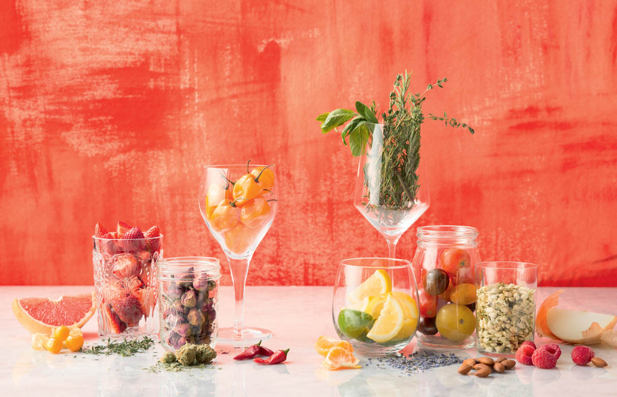 Decorative beauty shot (photo) of fruits, veggies, herbs in jars, spread on countertop, and in wine glasses.