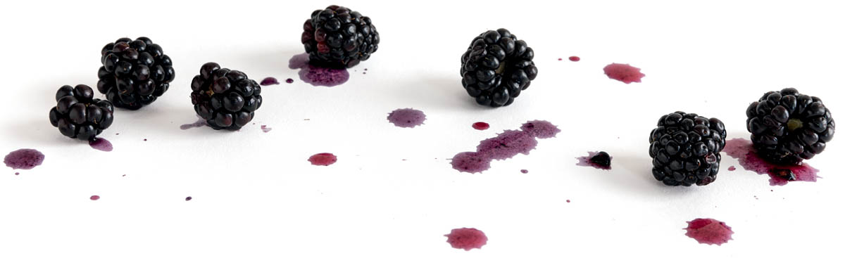 photo of blackberries on white surface, drips of their juices surround them.