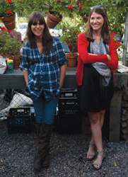 Two smiling young women standing at ease against a fence, their hands in their pockets.