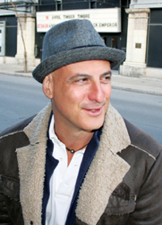 A smiling man in a felt hat and bomber jacket