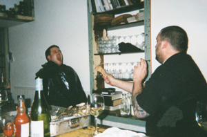 An weathered photo of a large man behind a bar slingshotting a piece of food towards his friend’s wide, waiting mouth