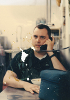 A weathered photo of a scowling man sitting in front of a bowl of cereal, talking on a corded phone coming out of the wall