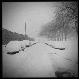 An old photo of a street and parked cars covered in several feet of snow