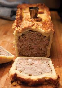 A view of the the end of a sliced Pate en Croute, the pink, meaty insides peeking through a frame of golden pastry