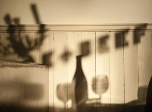 A white wood-paneled wall in a dim room, upon which a shadow is cast through the window of the Joe Beef restaurant, outlining the restaurant lettering along with a bottle and glasses of wine from a nearby table