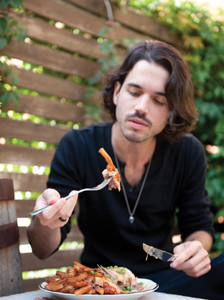 A young man with long hair eating a Hot Delicieux Sandwich outside