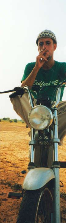 A young man on a scooter smoking a cigarette