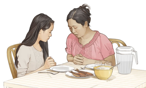 A mother says a prayer with her daughter before they eat a meal