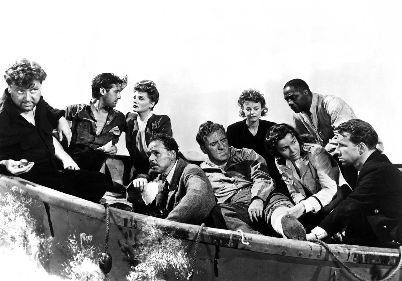 The image is from the Alfred Hitchcock movie “Lifeboat’ (1944).” It shows 7 men and 3 women from varying social class and race aboard a small boat. A young man and a young woman are looking into each other’s eyes. Another young woman is tending to a man whose leg is bandaged as she looks towards the young captain.