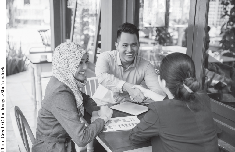 Photograph of a man and two women seated in front of a table, with the man and one of the women shaking hands.