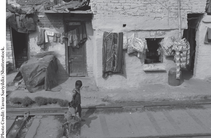 Photograph of a poor unhygienic neighborhood with mud houses near a railway track, depicting poverty.