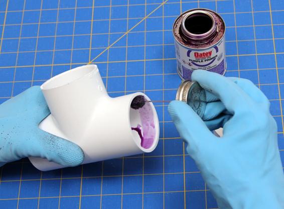 Apply purple primer to one end of the PVC tee and the outside of the pressure cap bushing.