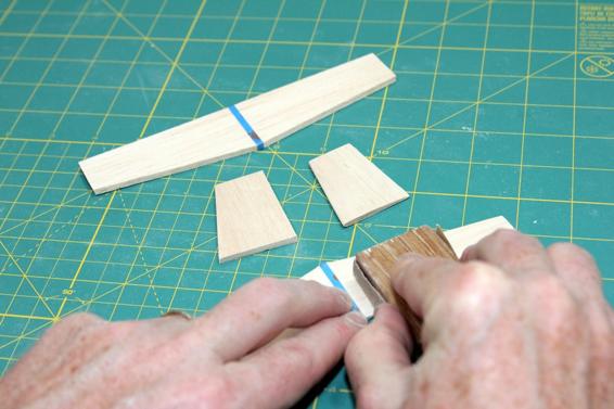 Sand the horizontal and vertical stabilizers with a neutral airfoil, like a fin. Keep the part of the horizontal stabilizer that will be glued to the fuselage and vertical stabilizer flat, protecting it with a thin strip of tape. Here you see two vertical stabilizers, one with an airfoil (right) and the other still flat (left).