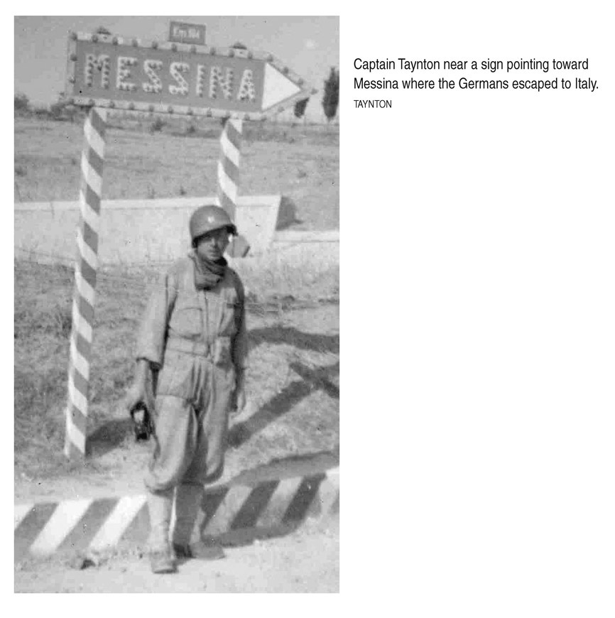 Captain Taynton near a sign pointing toward Messina where the Germans escaped to Italy. TAYNTON