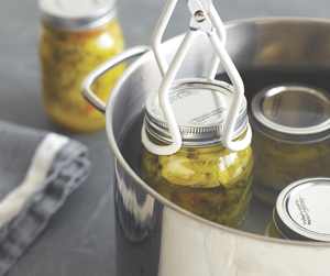 Removing full mason jars from a stockpot of water with pastic-coated tongs