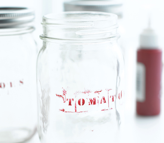 A glass jar with “Tomato” written in faded red stencil