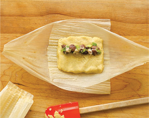 Spreading tamale filling into a corn husk