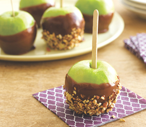 A nut- and caramel-covered green apple on a purple napkin