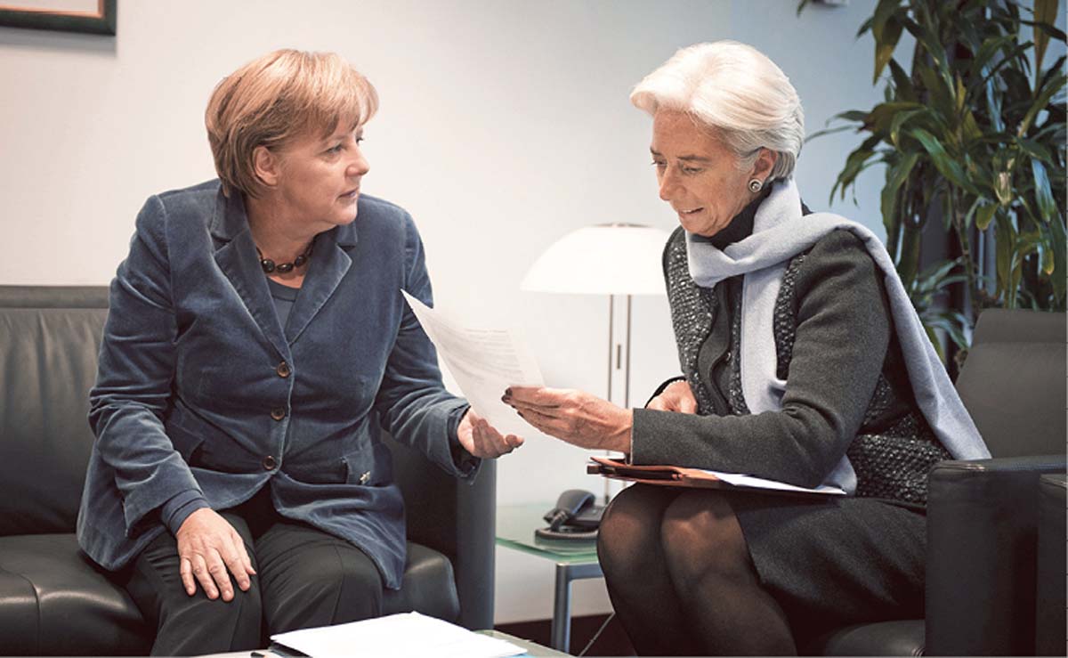 Angela Merkel und Christine Lagarde sitzen über Eck auf einer schwarzen Ledergarnitur, Merkel blickt Lagarde an, die auf ein Papier schaut, das sie in der Hand hält.