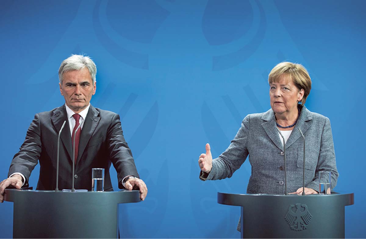 Werner Faymann und Angela Merkel stehen nebeneinander an zwei Rednerpulten, vor sich jeweils zwei Mikrofone