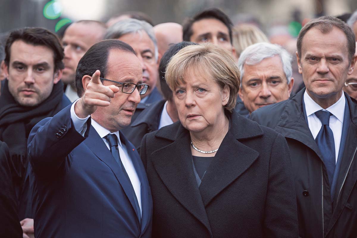 François Hollande Hollande, der nach vorn zeigt, und Angela Merkel stehen vor einer Menschenmenge, hinter ihnen zu erkennen ist Donald Tusk