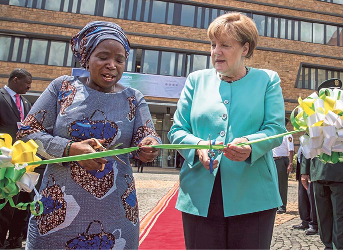 Angela Merkel steht neben Ellen Johnson Sirleaf unter einem Baldachin, im Hintergrund eine wehende Flagge Liberias und mehre Anzug tragende Männer