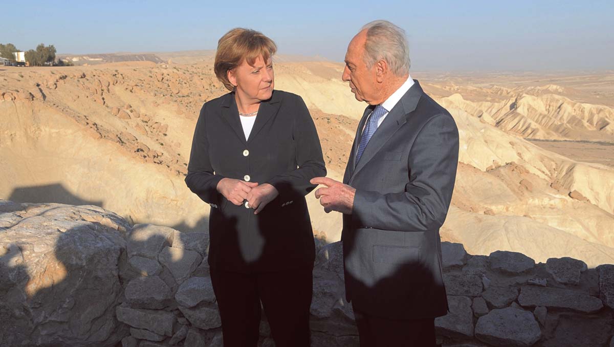 Angela blickt zu dem neben ihr stehenden Schimon Peres, hinter den beiden Wüste