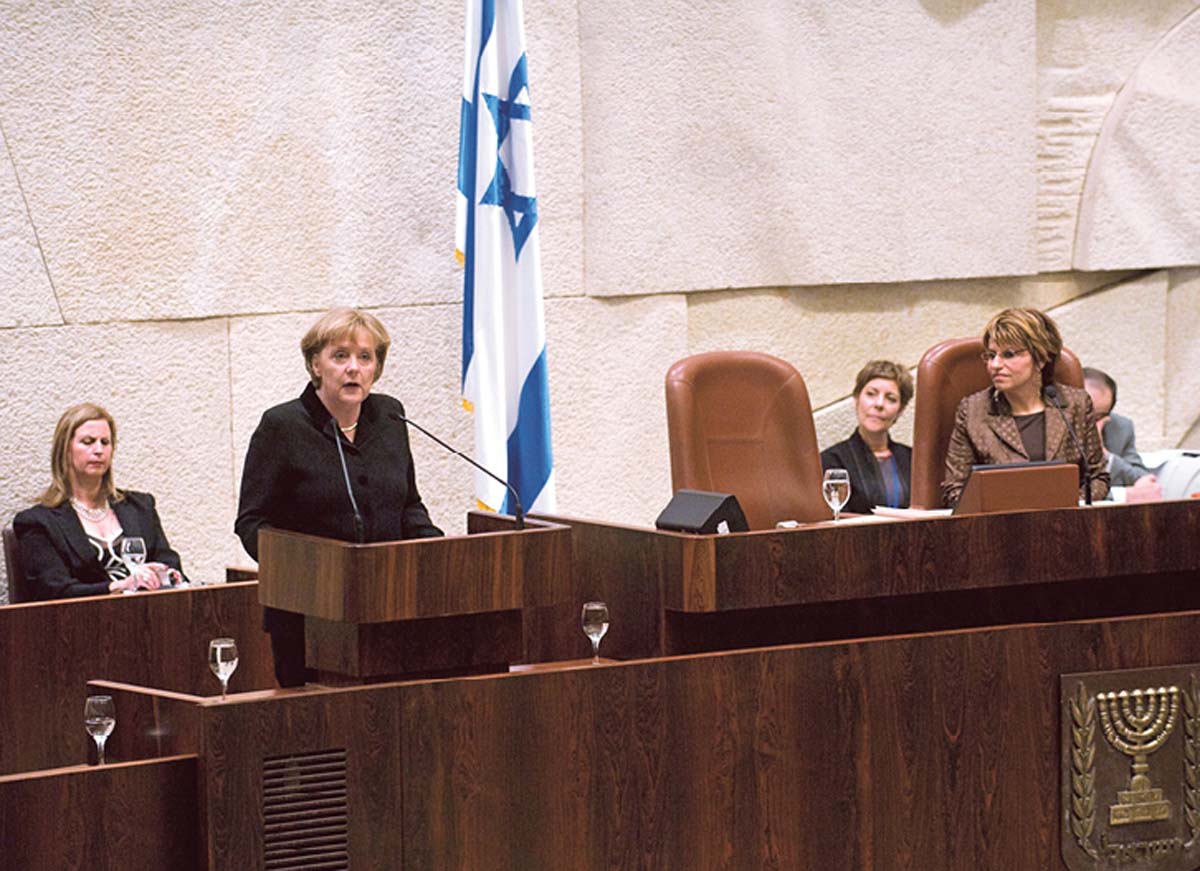 Angela Merkel steht an einem Rednerpult, der Platz neben ihr ist leer, daneben sitzt Dalia Itzik, im Hintergrund eine israelische Flagge