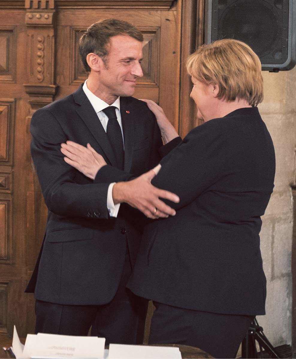 Emmanuel Macron und Angela Merkel blicken einander an und halten sich an den Armen