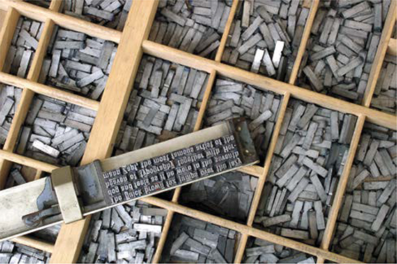 A stamp with its letters made of metal is shown over a backdrop having boxes of metal bars.